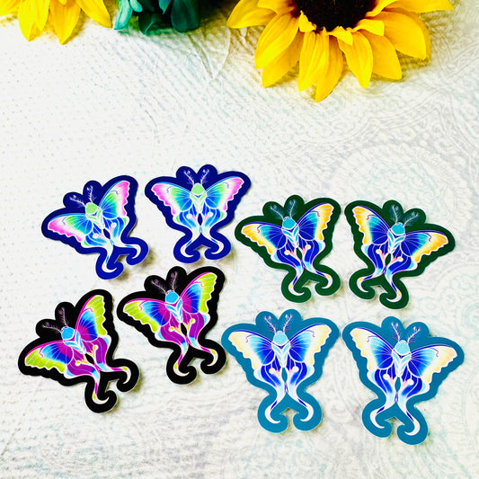 Colorful moth-shaped stickers on a textured white surface with sunflowers in the background.